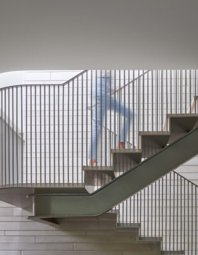 Person ascending a modern, curved staircase with metal railings in a well-lit interior space.